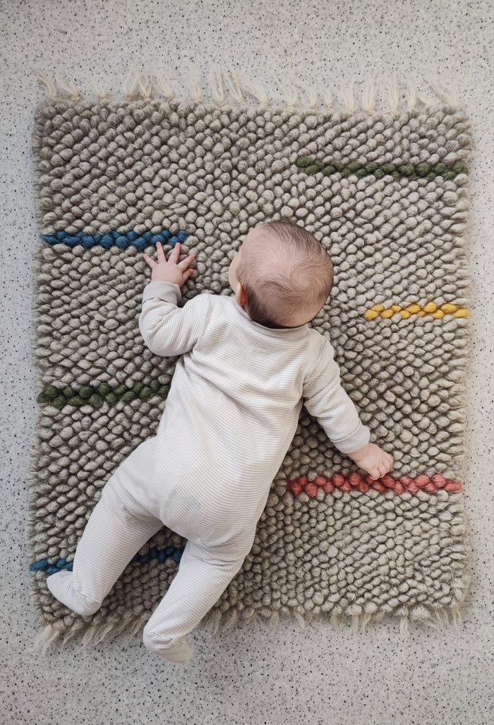 Child playing on the soft woolen Buzhok gray rainbow rug