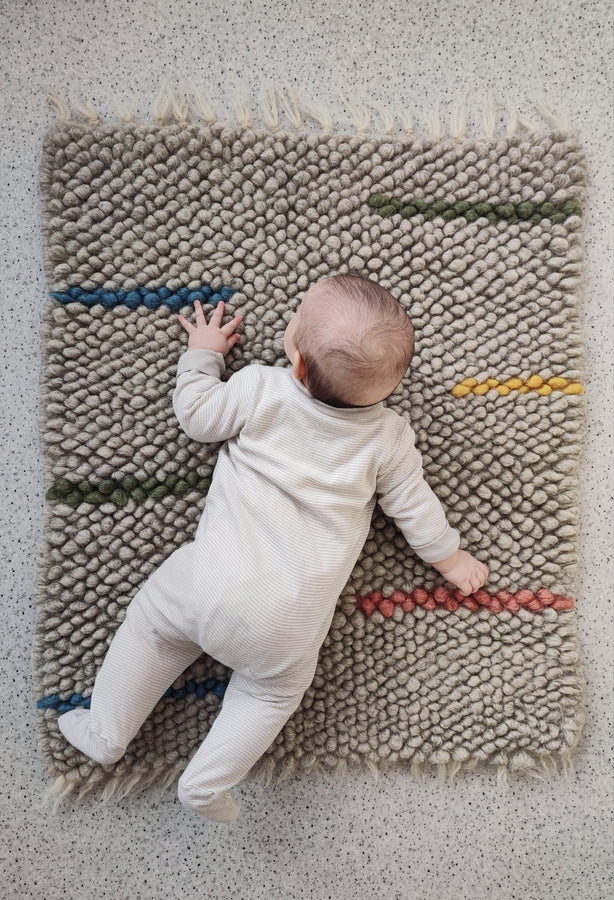 Child playing on the soft woolen Buzhok gray rainbow rug