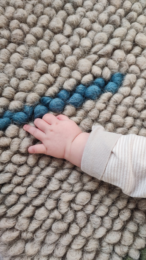 Child playing on the soft woolen Buzhok gray rainbow rug