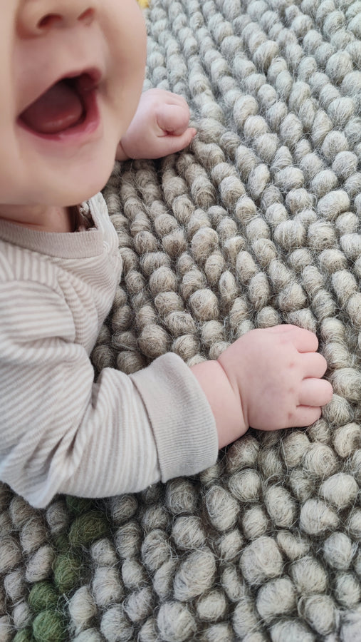 Happy child playing on the soft woolen Buzhok gray textured rug