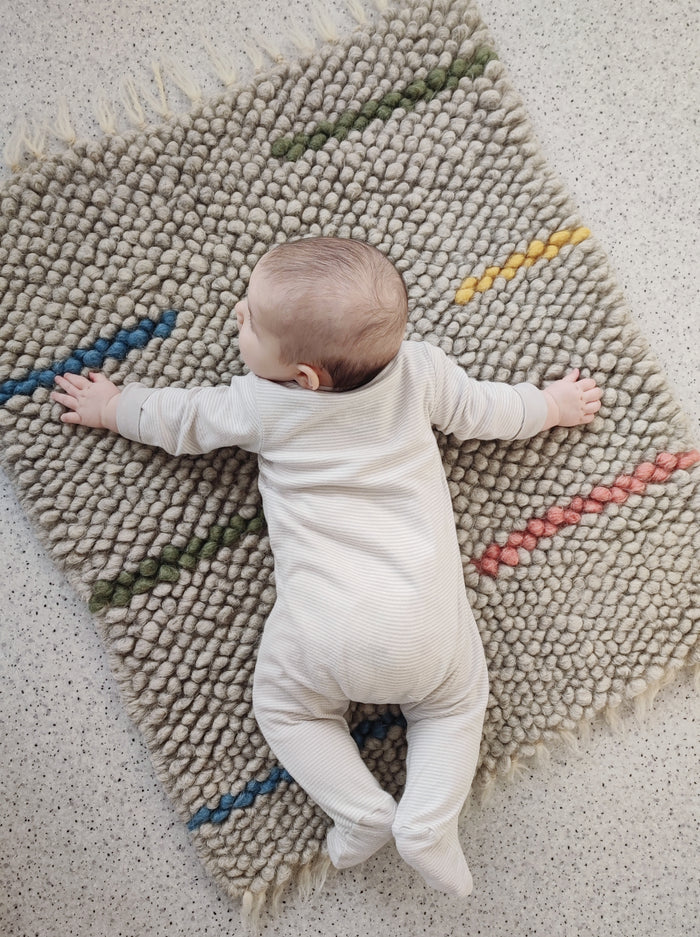 Child playing on the soft textured woolen Buzhok gray rainbow rug