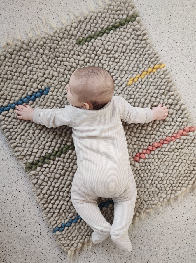 Child playing on the soft textured woolen Buzhok gray rainbow rug